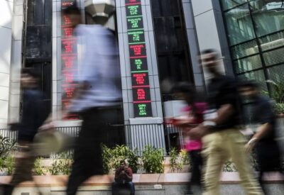 People walk past electronic boards displaying stock figures in the atrium of the National Stock Exchange of India, in Mumbai